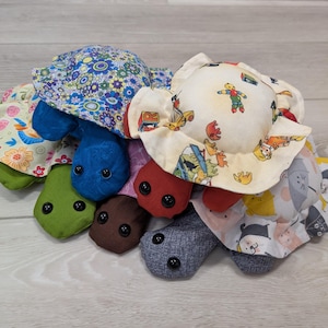 May include: A pile of handmade turtle plush toys. Each turtle has a different patterned fabric shell, including floral, cartoon, and geometric designs. The turtle bodies are various solid colours, with button eyes.