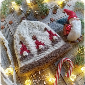 May include: A white knitted hat with a brown fur trim and a pattern of three gnomes wearing red hats and white beards. The hat is surrounded by Christmas decorations, including fairy lights, bells, and a candy cane.