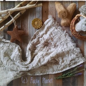 May include: A white linen throw blanket with a textured surface, a brown star-shaped bath sponge, a yellow soap bar, a basket with a white cloth, and lavender sprigs on a wooden background. (c) Flaxy Planet
