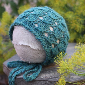 May include: A teal blue crocheted baby hat with a white fabric lining. The hat is sitting on a wooden surface.