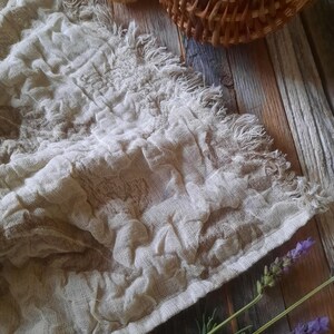 May include: A white linen tea towel with a frayed edge, laying on a rustic wooden surface with lavender sprigs.