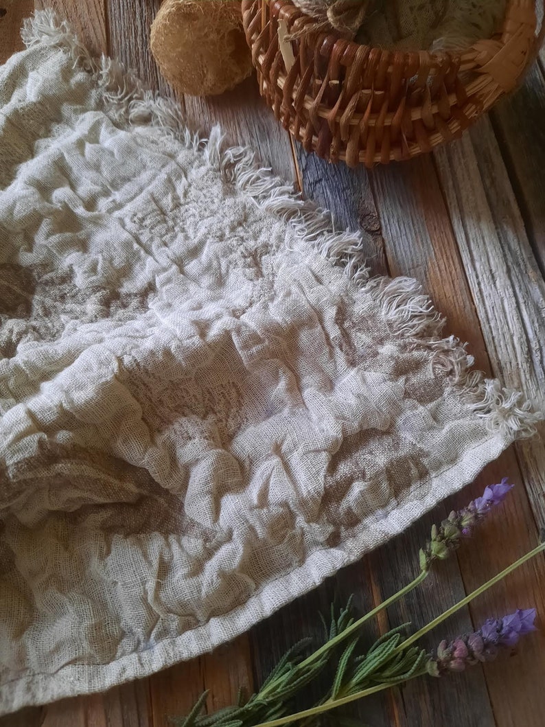 May include: A white linen tea towel with a frayed edge, laying on a rustic wooden surface with lavender sprigs.