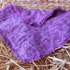 Puede incluir: Un pa&ntilde;uelo cuadrado de lino morado con un estampado floral y bordes deshilachados. El pa&ntilde;uelo se muestra sobre un lecho de paja, con una cesta de mimbre en el fondo. Las dimensiones del pa&ntilde;uelo no son visibles.