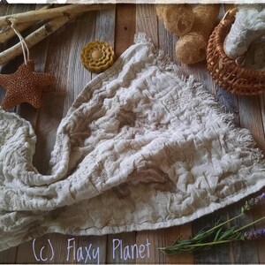May include: A white linen fabric with a textured surface and frayed edges. The fabric is laid out on a wooden surface with a variety of natural elements, including a starfish, a piece of soap, dried flowers, and a wicker basket. The text (c) Flaxy Planet is visible in the bottom right corner of the image.
