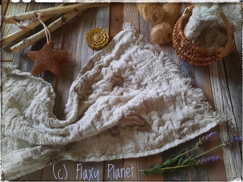 May include: A white linen fabric with a textured surface and frayed edges. The fabric is laid out on a wooden surface with a variety of natural elements, including a starfish, a piece of soap, dried flowers, and a wicker basket. The text (c) Flaxy Planet is visible in the bottom right corner of the image.