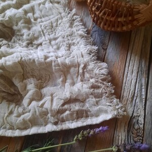 May include: A white linen tea towel with a fringed edge, lavender sprigs, and a wooden background.