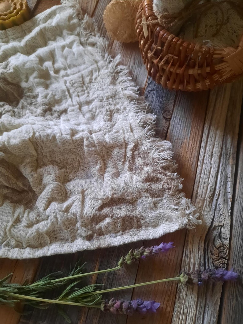 May include: A white linen tea towel with a fringed edge, lavender sprigs, and a wooden background.