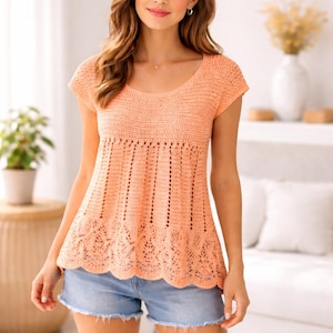 Puede incluir: Una blusa de crochet melocotón de manga corta con cuello redondo. La blusa presenta un diseño calado detallado alrededor de la cintura y un dobladillo festoneado. La prenda se combina con pantalones cortos vaqueros.