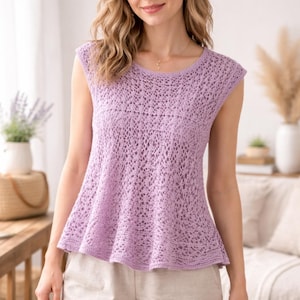 May include: A sleeveless, light purple crochet top with a round neckline and a flared peplum. The top features an open, lacy stitch pattern throughout. The model is wearing the top with light-colored pants.