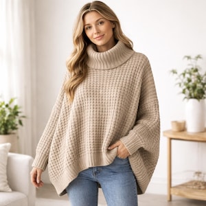 Puede incluir: Un suéter beige de cuello alto de gran tamaño con un patrón de punto de gofre. El suéter tiene mangas largas y un ajuste relajado. La modelo lleva vaqueros azules. El suéter es de color neutro, adecuado para varios conjuntos.