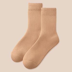 Puede incluir: Un par de calcetines de color beige. Los calcetines están hechos de un material suave y tienen puños acanalados. Los calcetines son de un color neutro y serían adecuados para el uso diario. Los calcetines se muestran sobre un fondo beige claro.