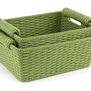 Puede incluir: Dos cestas de almacenamiento verdes tejidas, una anidada dentro de la otra. Cada cesta tiene forma rectangular con asas redondeadas. Las cestas son de color verde claro y tienen un aspecto texturizado y tejido.