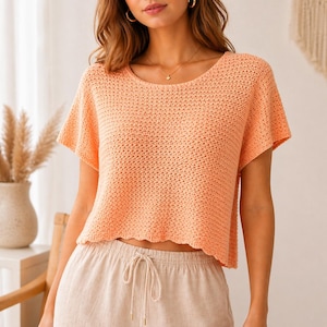 Può includere: Un top all'uncinetto color pesca, a maniche corte, con scollatura rotonda e orlo leggermente smerlato. Il top è realizzato in un tessuto strutturato a trama aperta. La modella indossa pantaloni beige con coulisse.