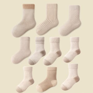 Könnte beinhalten: Neun Paar Socken in Beige- und Brauntönen. Die Socken weisen unterschiedliche Texturen auf, darunter gerippte und glatte Designs. Einige Socken haben farblich abgesetzte Zehen und Bündchen.