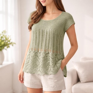 May include: A light green crochet top with short sleeves and a round neckline. The top features a detailed openwork design on the bodice and a scalloped hem. Paired with light-colored shorts, the top is a casual, handmade garment.