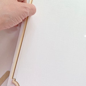 Pu&ograve; includere: Una superficie bianca con una cornice in legno che viene fissata ad essa. La cornice ha un bordo decorativo con angoli arrotondati.