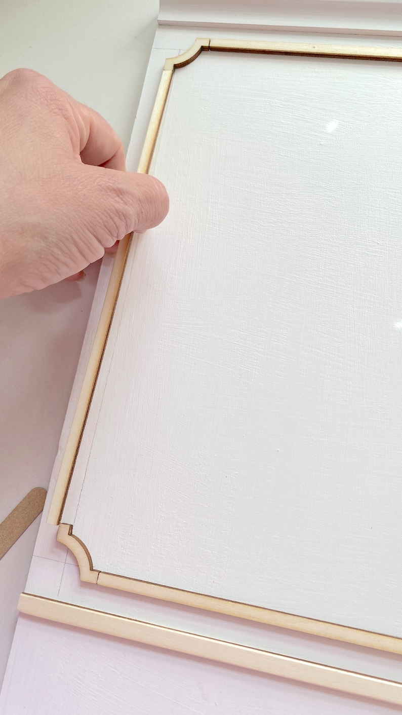 Pu&ograve; includere: Una superficie bianca con una cornice in legno che viene fissata ad essa. La cornice ha un bordo decorativo con angoli arrotondati.
