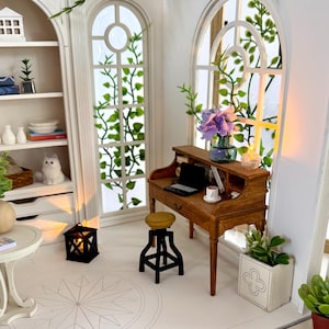 May include: Miniature dollhouse interior with a wooden desk, stool, and bookshelf. The room features arched windows with green vines, a small table, and a decorative lantern. A laptop and a cup sit on the desk. The room is painted white.