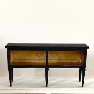 Peut inclure: Un meuble noir rectangulaire avec quatre pieds effilés. L'intérieur est doré avec un motif en forme de losange. Le meuble a un design simple et élégant, adapté à divers styles de décoration.