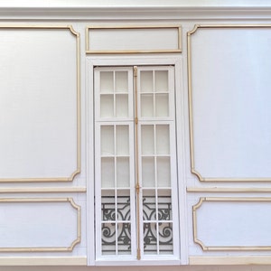 Pu&ograve; includere: Un muro bianco con una grande finestra incorniciata in legno. La finestra ha pi&ugrave; pannelli di vetro e una griglia di metallo decorativa. Il muro &egrave; diviso in sezioni da modanature in legno decorative.