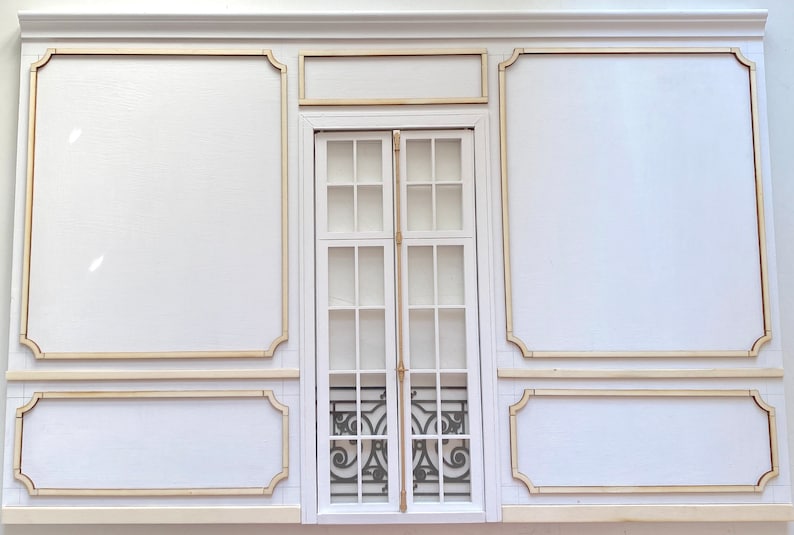 Pu&ograve; includere: Un muro bianco con una grande finestra incorniciata in legno. La finestra ha pi&ugrave; pannelli di vetro e una griglia di metallo decorativa. Il muro &egrave; diviso in sezioni da modanature in legno decorative.