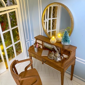 May include: Miniature wooden desk with a round mirror, chair, and accessories. The desk features a small teapot, teacup, and books. A small Christmas tree and two decorative lights sit on the desk. The chair has a curved back and legs. The room has light blue walls.
