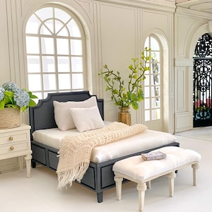 Pu&ograve; includere: Una scena di camera da letto in miniatura con un letto grigio scuro, biancheria da letto bianca e una coperta con frange color crema. Un piccolo comodino bianco contiene un cesto di ortensie blu. Una panca abbinata si trova ai piedi del letto. La stanza ha grandi finestre ad arco.