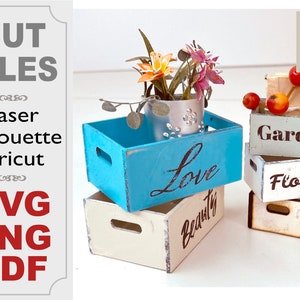 May include: Four miniature wooden crates with different painted designs. The top crate is blue and says "Love". The crate below it is white and says "Beauty". The crate on the right is green and says "Garden" and the crate below it is white and says "Flowers".