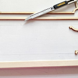 Pu&ograve; includere: Una superficie bianca con una cornice in legno e modanature decorative. Un coltello multiuso &egrave; posizionato sopra la cornice.