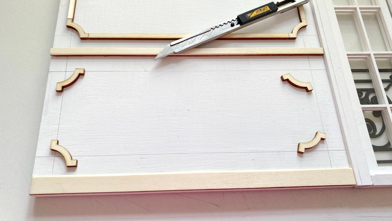 Pu&ograve; includere: Una superficie bianca con una cornice in legno e modanature decorative. Un coltello multiuso &egrave; posizionato sopra la cornice.