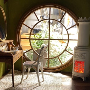 May include: A miniature room scene featuring a wooden desk with a mirror, a white chair, and a decorative white stove. A large round window offers a view of the outside. The room has a cozy, inviting atmosphere.