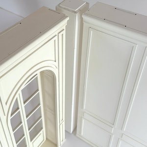 May include: A set of two off-white architectural wall panels featuring a matte finish. One panel displays a tall arched doorway with a multi-pane window design, while the other panel features a rectangular grid pattern with raised molding details.