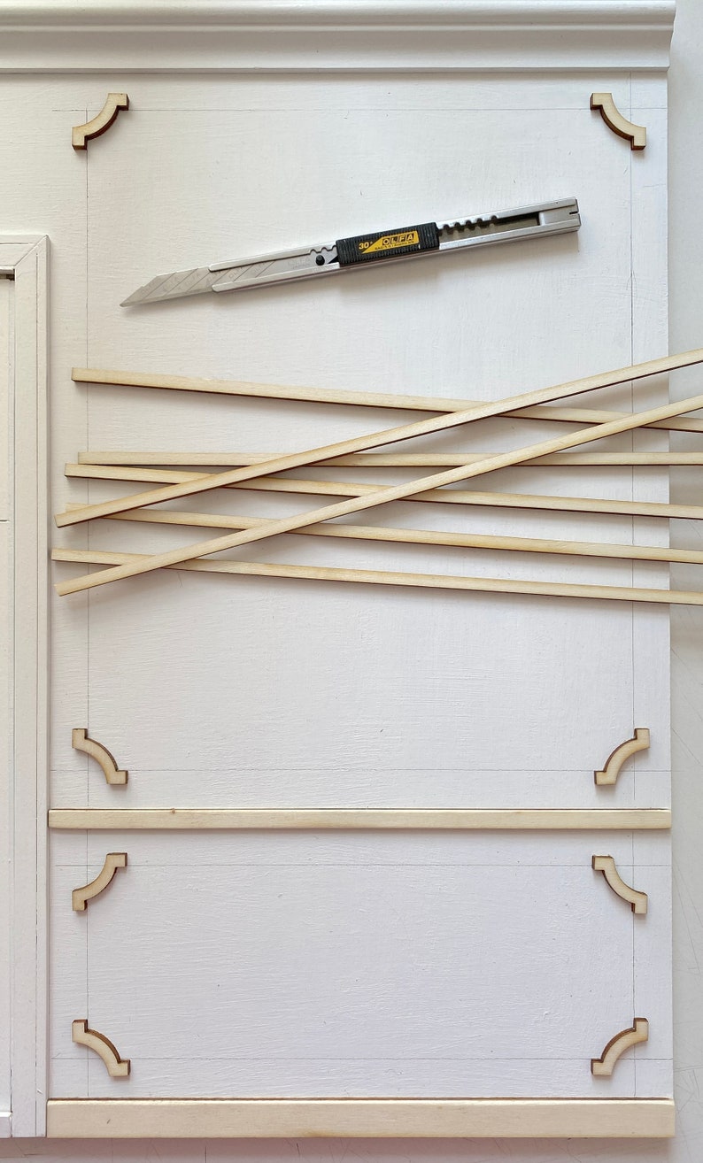 Pu&ograve; includere: Una superficie bianca con un disegno a matita di una cornice. Ci sono strisce di legno e un coltello multiuso sulla superficie. Il coltello multiuso ha la scritta "OLFA" su di esso.