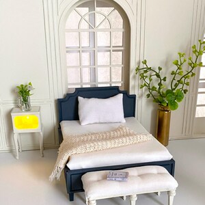 Pu&ograve; includere: Set da camera da letto in miniatura con un letto blu navy, biancheria da letto bianca e una coperta color crema. Una panca bianca si trova ai piedi del letto e un piccolo comodino con luce gialla &egrave; a sinistra. Un vaso con verde &egrave; a destra.