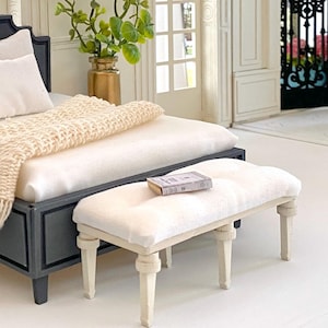 Pu&ograve; includere: Scena di camera da letto in miniatura con un letto con struttura grigio scuro, biancheria da letto bianca e una coperta lavorata a maglia color crema. Una piccola panca imbottita con un libro poggia ai piedi del letto. Un vaso dorato con vegetazione &egrave; visibile.