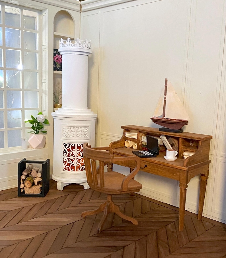 May include: Miniature wooden desk with a small sailboat, laptop, and books. A wooden chair sits in front of the desk. A white fireplace and a window with a plant are in the background. The floor has a herringbone pattern.