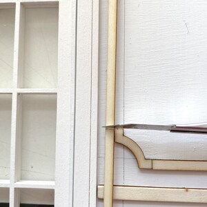 Pu&ograve; includere: Primo piano di una cornice in legno in fase di assemblaggio. La cornice &egrave; in legno chiaro e ha un design semplice. La cornice &egrave; assemblata su una superficie bianca.