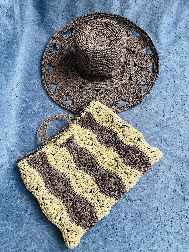 May include: A crocheted sun hat and handbag set. The hat is brown with a wide brim and circular accents. The handbag features a wavy pattern in cream and brown, with clear handles. The set is designed for summer.