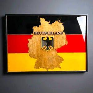 Könnte beinhalten: Ein gerahmtes Kunstwerk mit der deutschen Flagge. Das Design zeigt schwarze, rote und gelbe Streifen. In der Mitte befindet sich eine Holzkarte Deutschlands mit dem Wort "DEUTSCHLAND" und einem Wappen.
