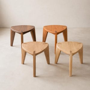 May include: Four wooden stools with triangular seats and three legs each. The stools are in various wood tones, including dark brown, light brown, and natural wood. The stools are simple and modern in design.