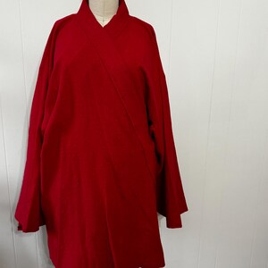 May include: A vibrant red, long-sleeved garment with a wrap-style front, displayed on a mannequin. The fabric appears to be a medium-weight material, with a subtle sheen. The design features a wide collar and a relaxed fit, suitable for layering.
