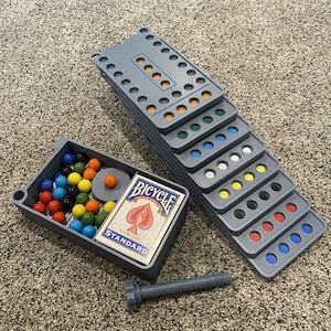 May include: A gray board game set with colorful marbles, a deck of Bicycle playing cards, and a gray bolt. The game boards have colored circles. The marbles are in a gray tray.