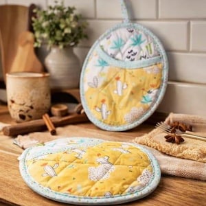 May include: Two quilted, oval-shaped pot holders. One is hanging, the other is lying flat. Both have a yellow cactus print on the bottom half and a white and teal leaf print on the top half. The edges are trimmed with a light blue fabric.