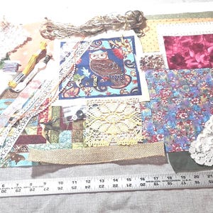 May include: A craft supply assortment featuring fabric scraps with floral and owl patterns, white lace trim, burlap ribbon, embroidery floss, and a metal ruler showing measurements up to 26 inches. The collection includes various textures and colors.