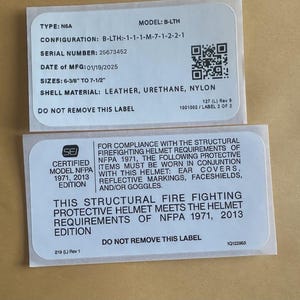 Puede incluir: Dos etiquetas blancas con texto negro que detallan las especificaciones de un casco de protección contra incendios estructural. La información incluye modelo, número de serie, fecha de fabricación, tamaños (16,2 cm a 19,1 cm) y material de la carcasa (cuero, uretano, nailon).