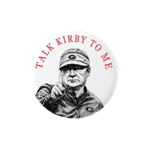 May include: A circular button featuring a black and white sketch of a person wearing a visor and jacket with a logo, pointing a finger upward. The red text TALK KIRBY TO ME is arched over the top of the illustration on a plain white background.