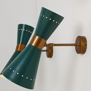 May include: A pair of teal wall sconces with a conical shade design. Each sconce features a brass-colored band and a series of small, evenly spaced holes along the top. The sconces are mounted on a brass-colored arm and base.