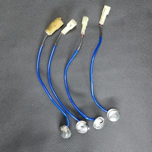 May include: Four automotive sensors with blue wires, silver heads, and white connectors. One sensor has a tan foam covering. The sensors are arranged on a dark gray surface.