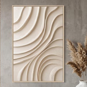 May include: A framed abstract wall art piece featuring a textured, cream-colored design of flowing, curved lines. The artwork is encased in a light brown wooden frame, creating a modern and minimalist aesthetic. The piece is displayed against a neutral gray wall.