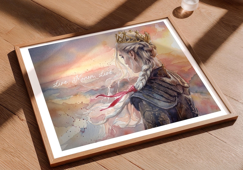 May include: Watercolor art print in a wooden frame. The artwork depicts a woman with a crown and a long braid, set against a sunset backdrop. The text "Live, Manon, Live" is written across the image. The color palette includes shades of pink, orange, and blue.